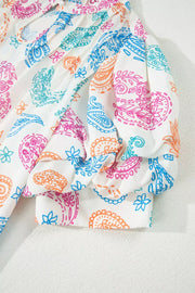 White maternity blouse with vibrant paisley print, puff sleeves, and frill detail.