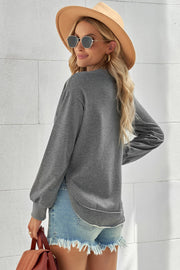 Gray sweatshirt with asymmetric hemline and long sleeves, styled with denim shorts.