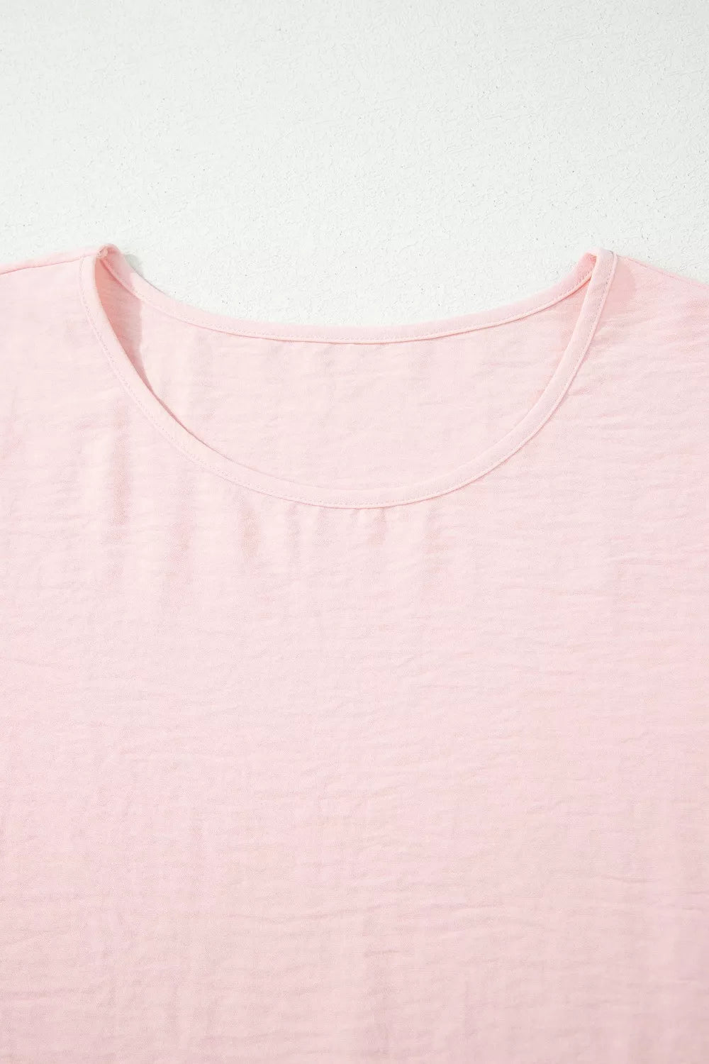 Blush pink polyester blouse with short sleeves and a ruffled neckline.