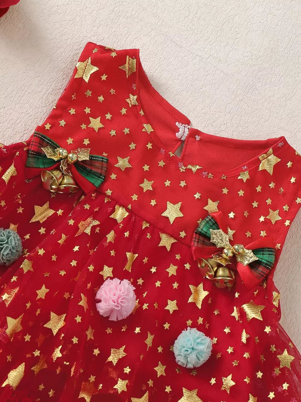Red baby dress with gold stars, pom-poms, and bell details.