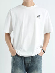 Men's white cotton graphic tee with small chest print and relaxed fit.