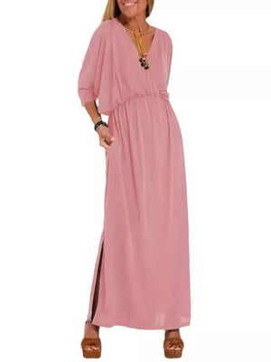 Pink V-neck maxi dress with dolman sleeves and side slits, cinched waist, worn with necklace.