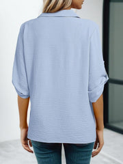 Light blue textured blouse with roll-up sleeves and button detail.