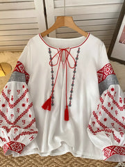 White embroidered folk shirt with tie neck and red tassel details.