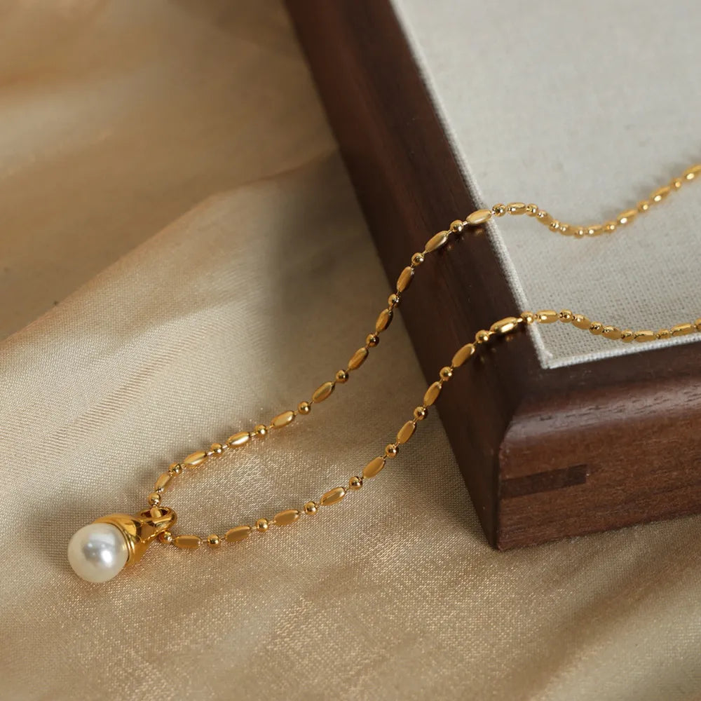 Gold pearl drop necklace with a delicate chain and oval bead accents.
