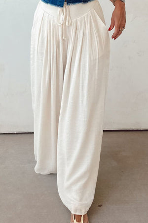 White pleated linen palazzo trousers with drawstring waist and pockets.