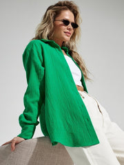 Green textured cotton overshirt with relaxed fit and button front, styled with white top and beige pants.