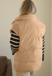 Padded tan sleeveless hooded vest with pockets, worn over a striped sweater.