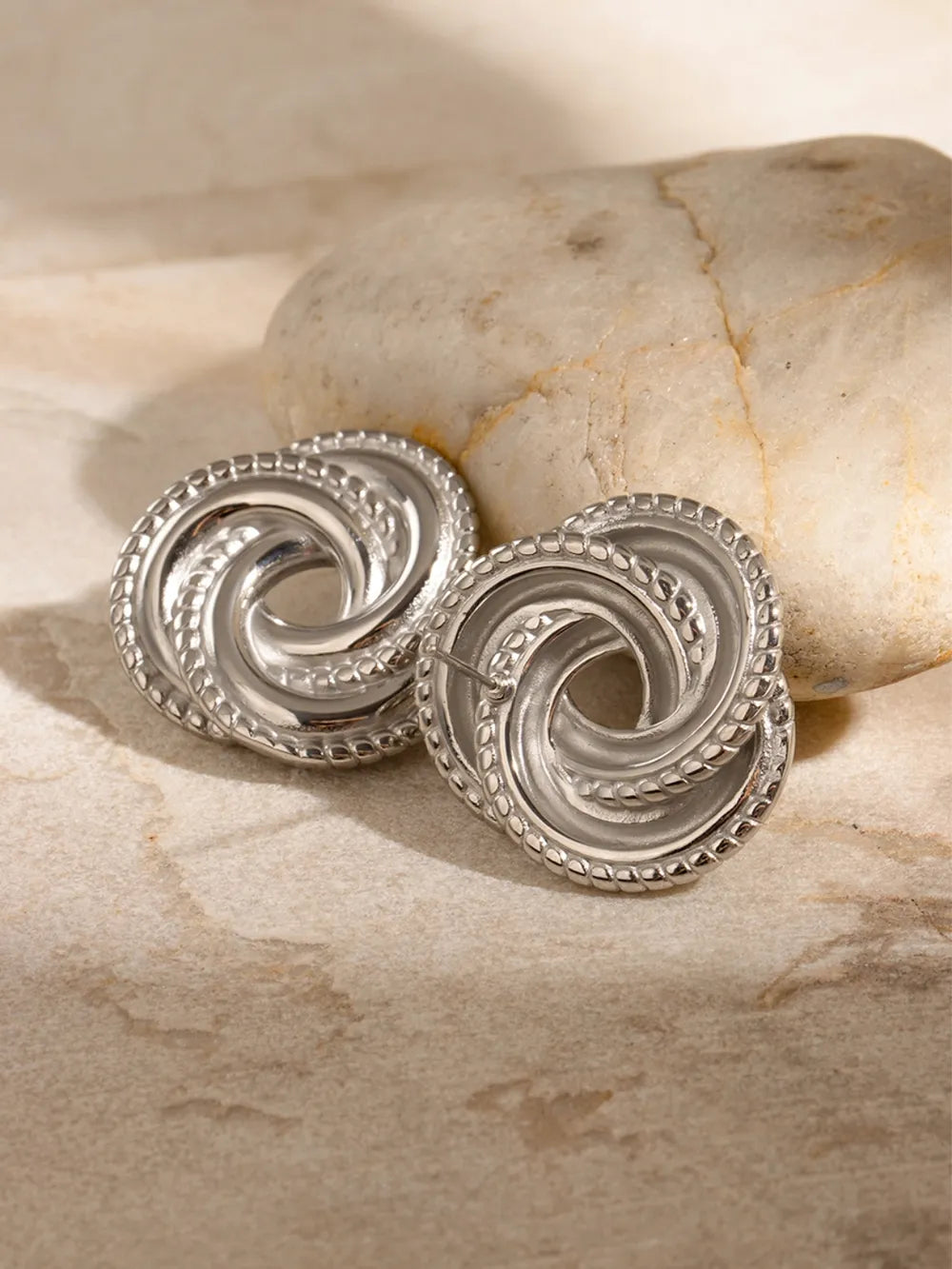 Silver swirl knot stud earrings with textured border detail
