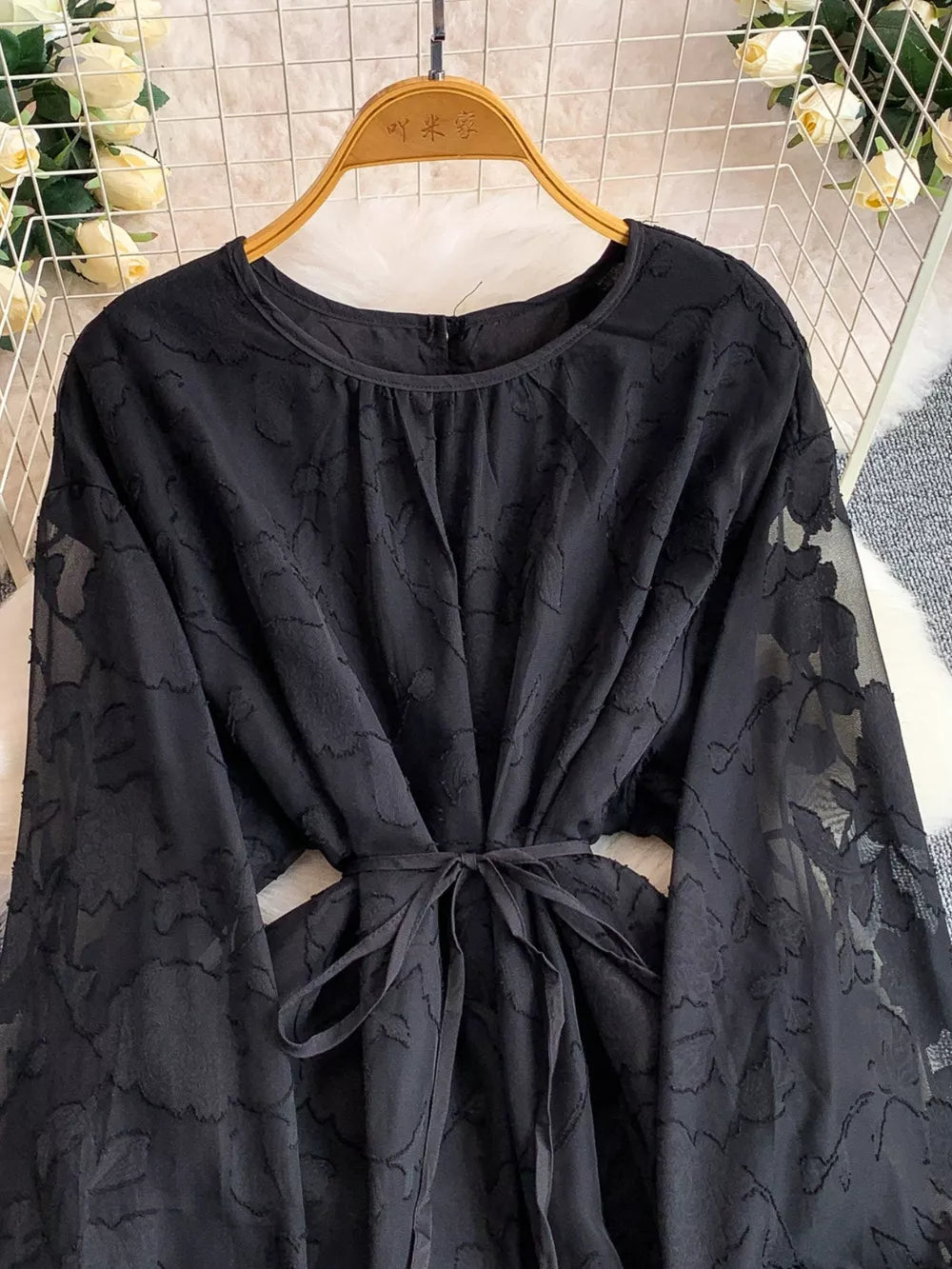 Black embroidered tie-waist dress with sheer floral sleeves and round neckline.
