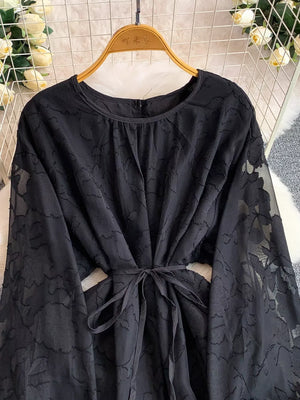 Black embroidered tie-waist dress with sheer floral sleeves and round neckline.