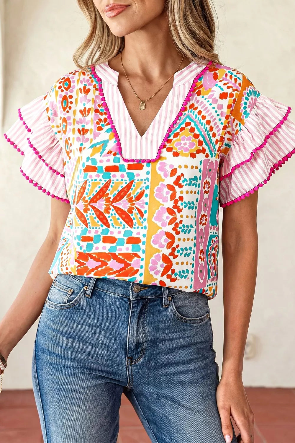 Vibrant patchwork ruffle blouse with pink striped sleeves and pom pom trim.