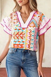 Vibrant patchwork ruffle blouse with pink striped sleeves and pom pom trim.