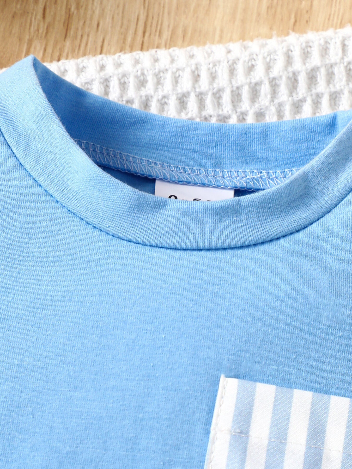 Pastel blue cotton baby tee with striped pocket detail.