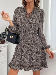 Ruffled tie neck floral mini dress in dark brown with long sleeves and tiered skirt.