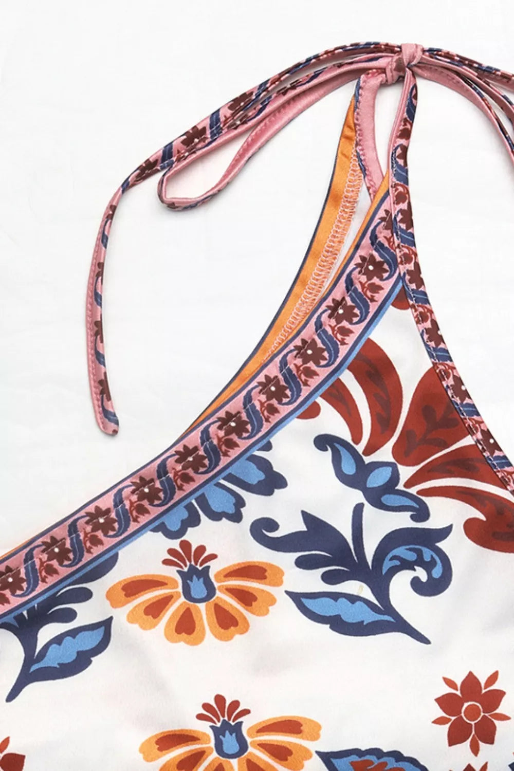 Vibrant floral one-shoulder bodysuit with tie straps and colorful trim.