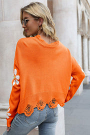 Orange distressed knit sweater with daisy appliqué on sleeves and frayed hem.