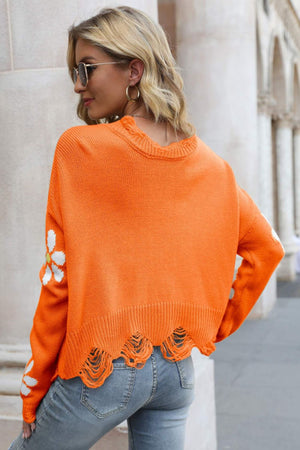 Orange distressed knit sweater with daisy appliqué on sleeves and frayed hem.