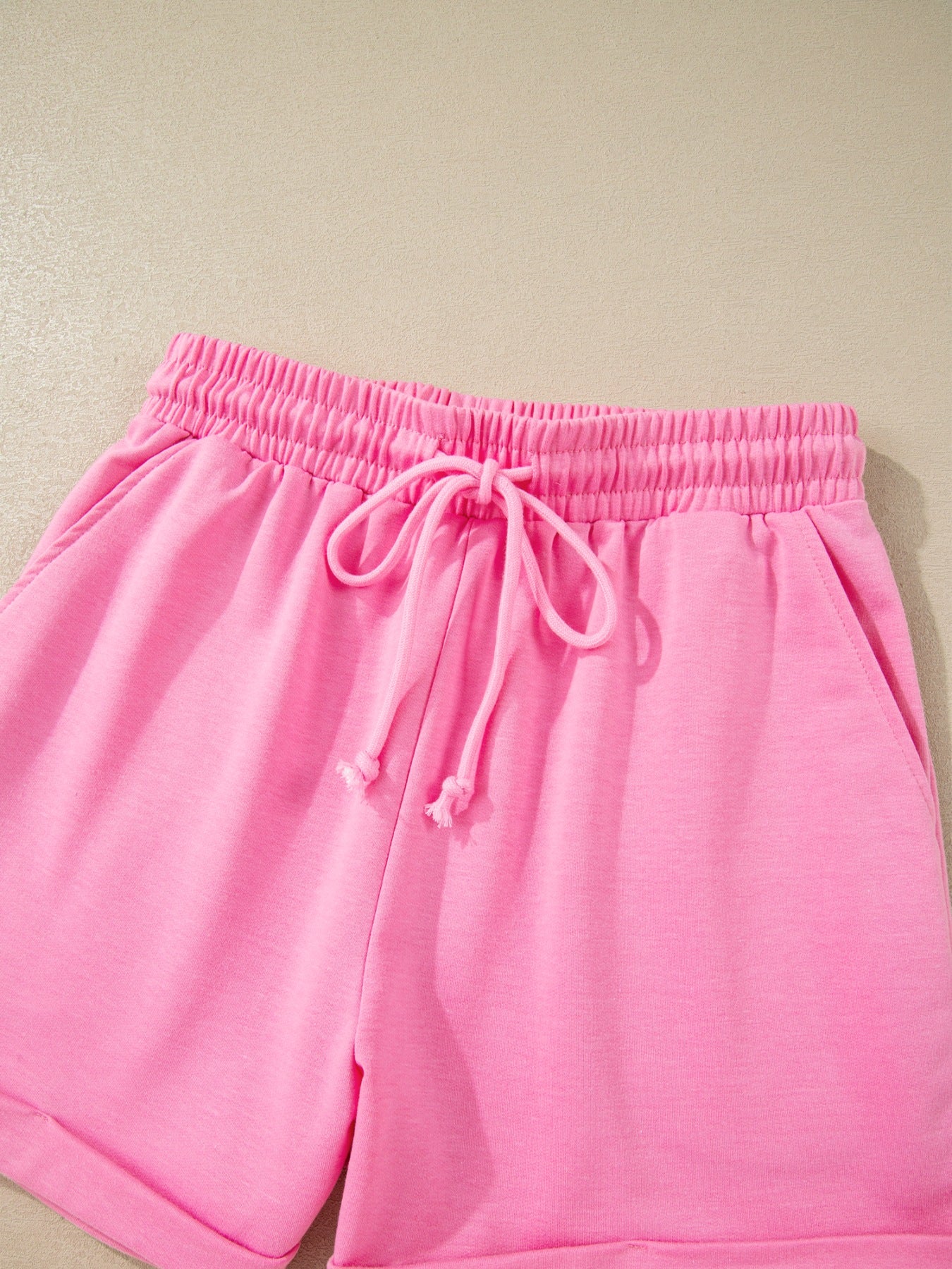 Pink cotton drawstring shorts with elastic waistband and cuffed hem.