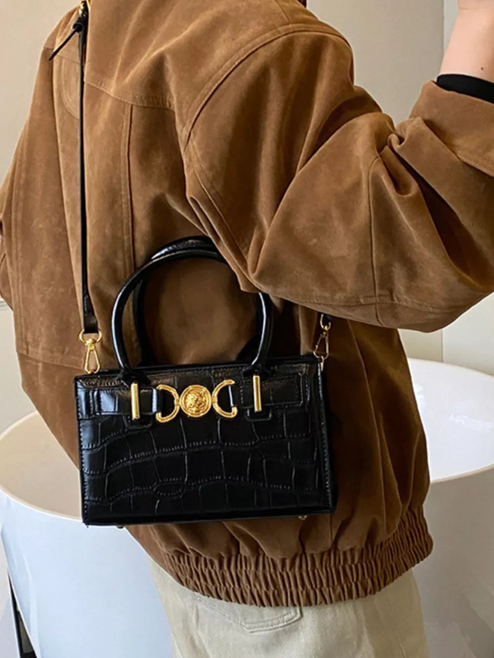 Black crocodile-textured crossbody bag with gold hardware and top handle.