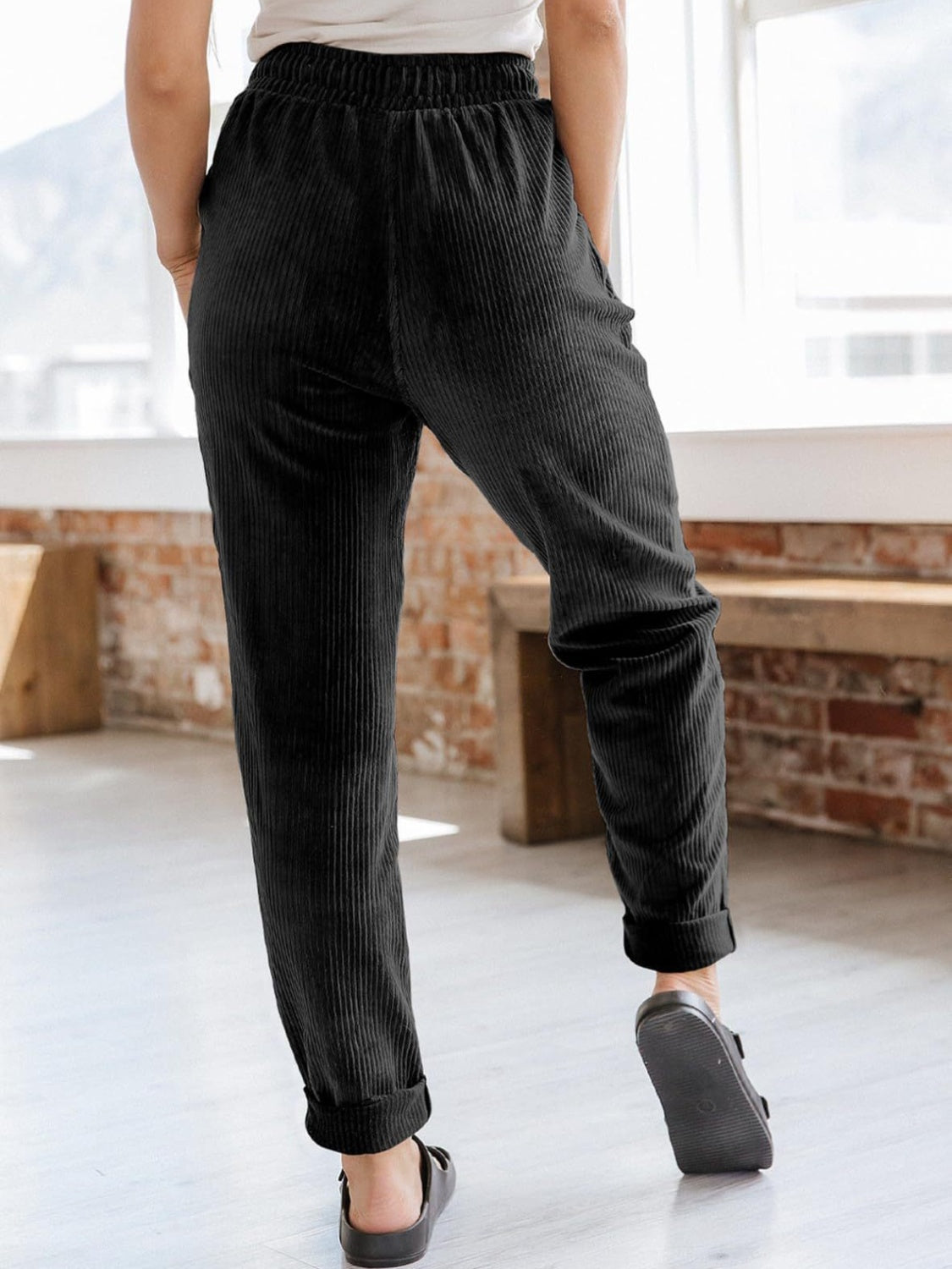 Black corduroy tapered trousers with drawstring waist and cuffed hem.