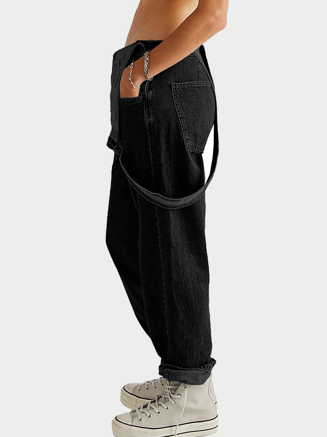 Black denim overalls with cross-back straps and cuffed hems, styled casually.
