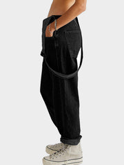 Black denim overalls with cross-back straps and cuffed hems, styled casually.
