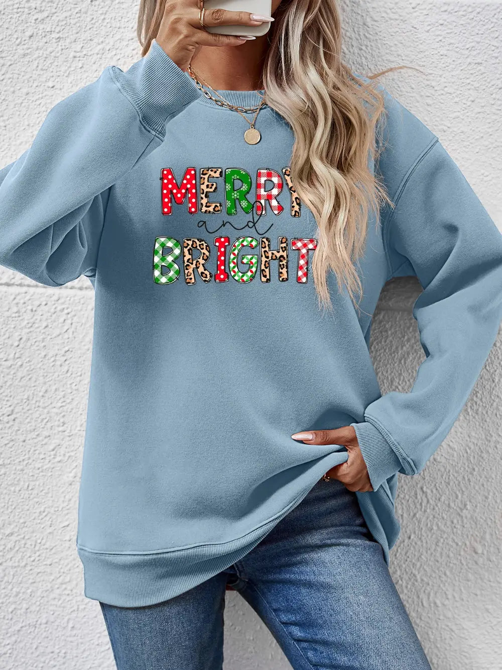 Light blue crewneck sweatshirt with "Merry and Bright" graphic in festive patterns.