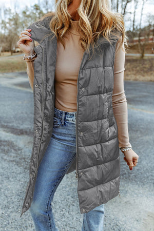 Longline hooded puffer vest in charcoal with zip and snap closure, styled with jeans.