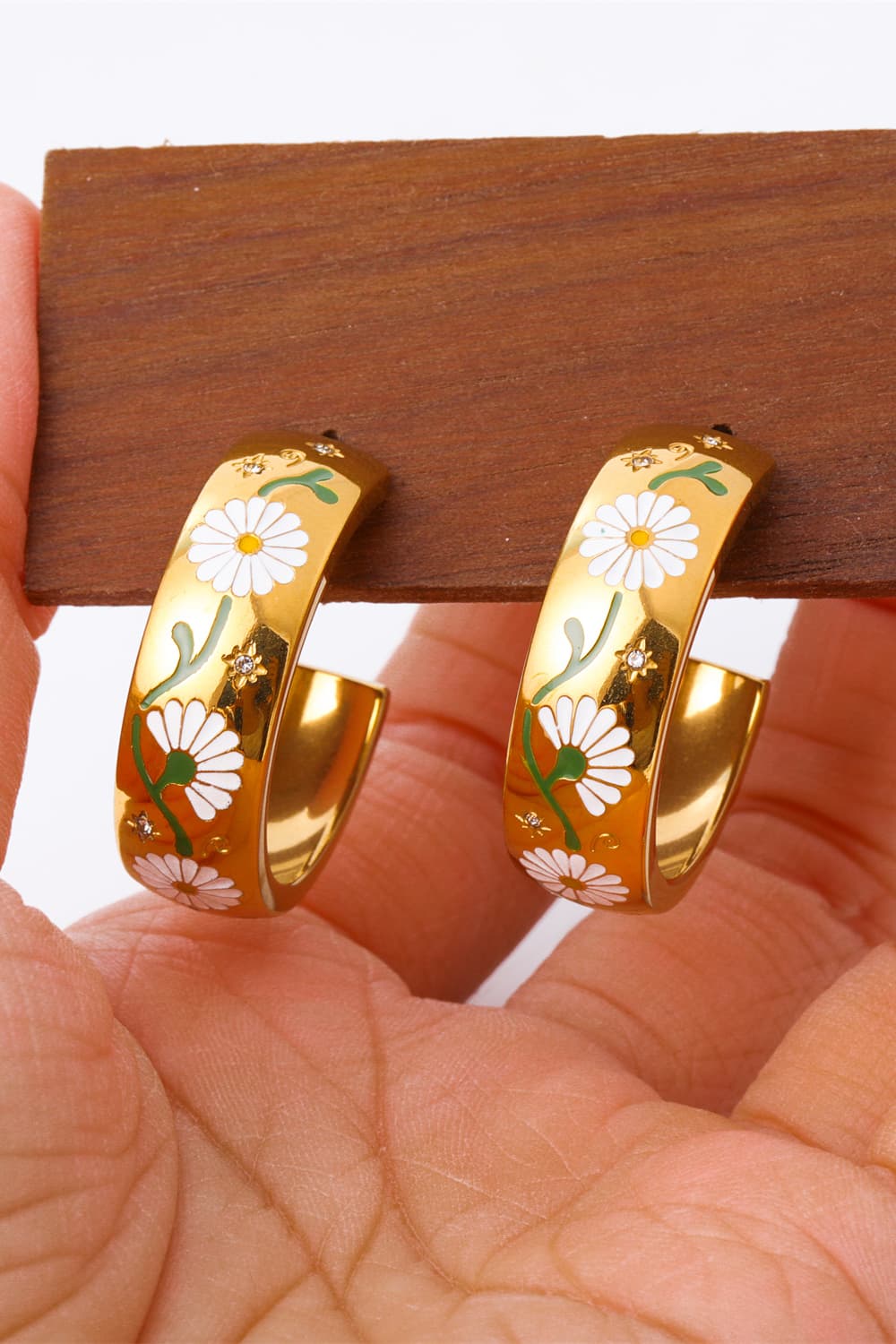 Gold hoop earrings with white daisy floral enamel pattern and green stems.