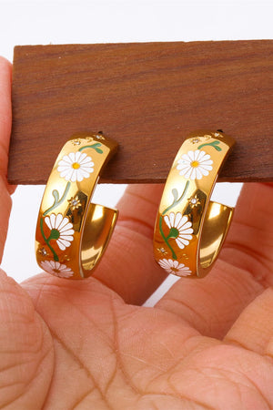 Gold hoop earrings with white daisy floral enamel pattern and green stems.