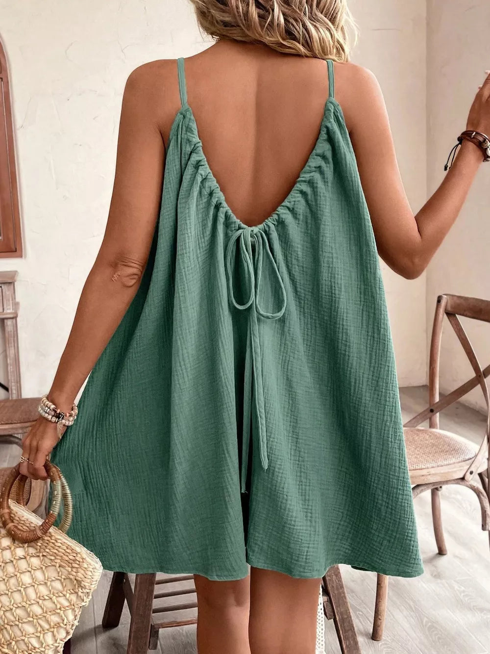 Spaghetti strap mini dress in green with a back tie detail and textured fabric.