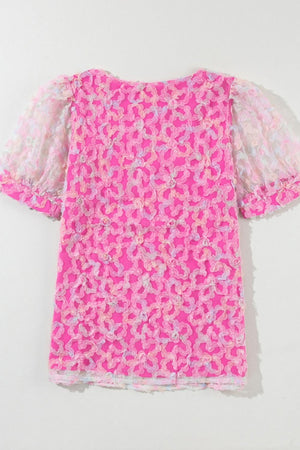 Fuchsia pink blouse with floral appliqué and sheer puff sleeves.