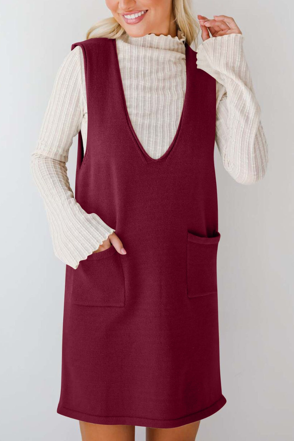Burgundy knit sweater dress with deep V-neck and two front pockets, styled over a cream ribbed turtleneck.