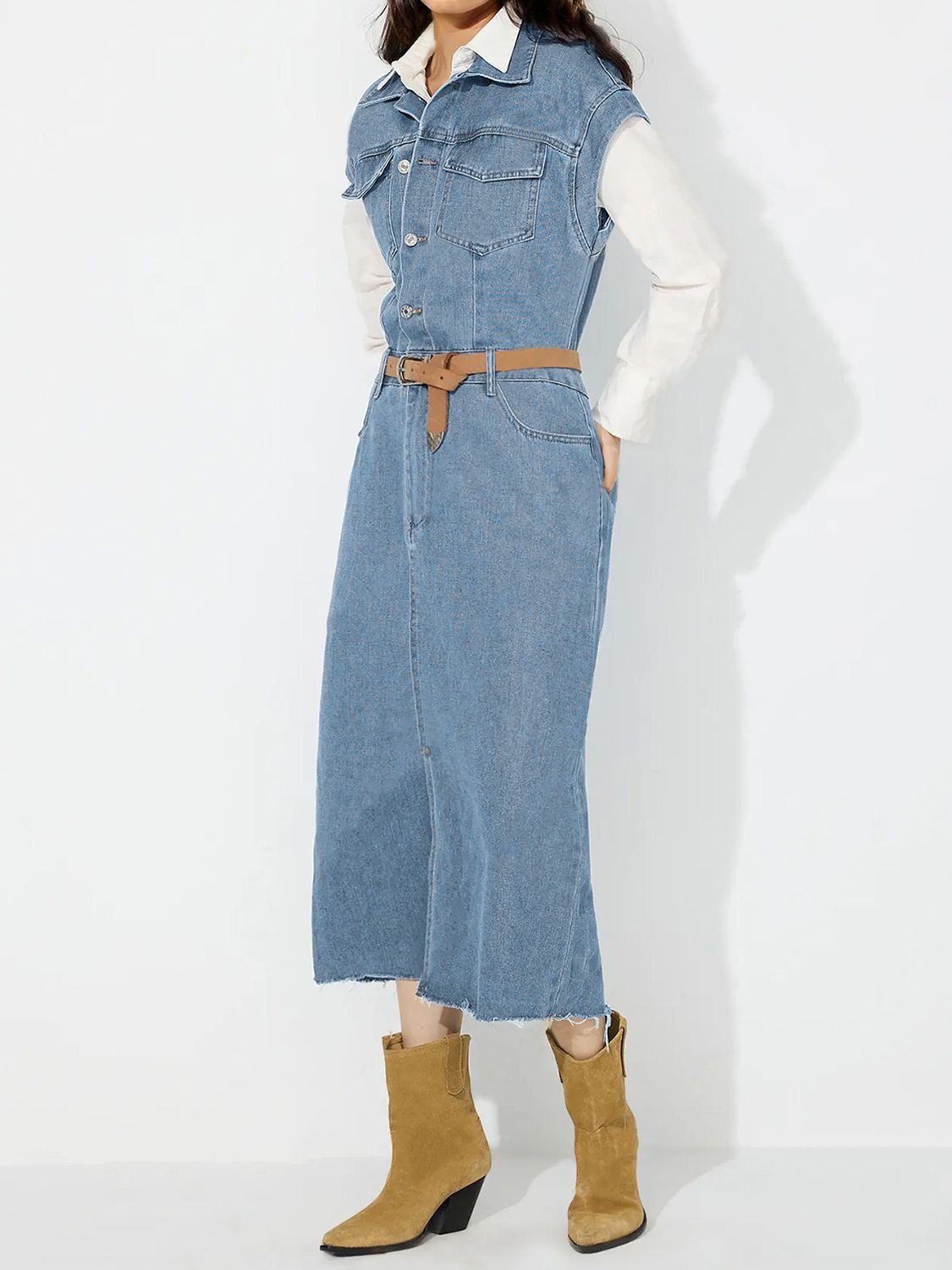 Sleeveless light wash denim midi dress with slit and button front, cinched with a brown belt.
