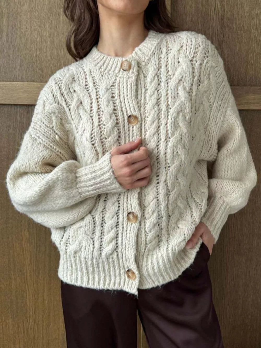 Ivory cable-knit button-down cardigan with round neckline and wooden buttons.