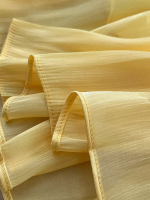 Yellow pleated maxi skirt fabric detail with subtle vertical texture and stitched hem.