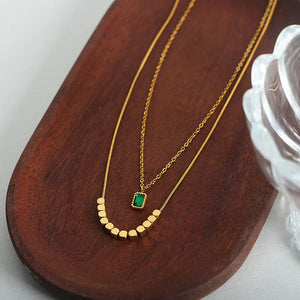 Gold layered necklace with emerald cube pendant and bead accents