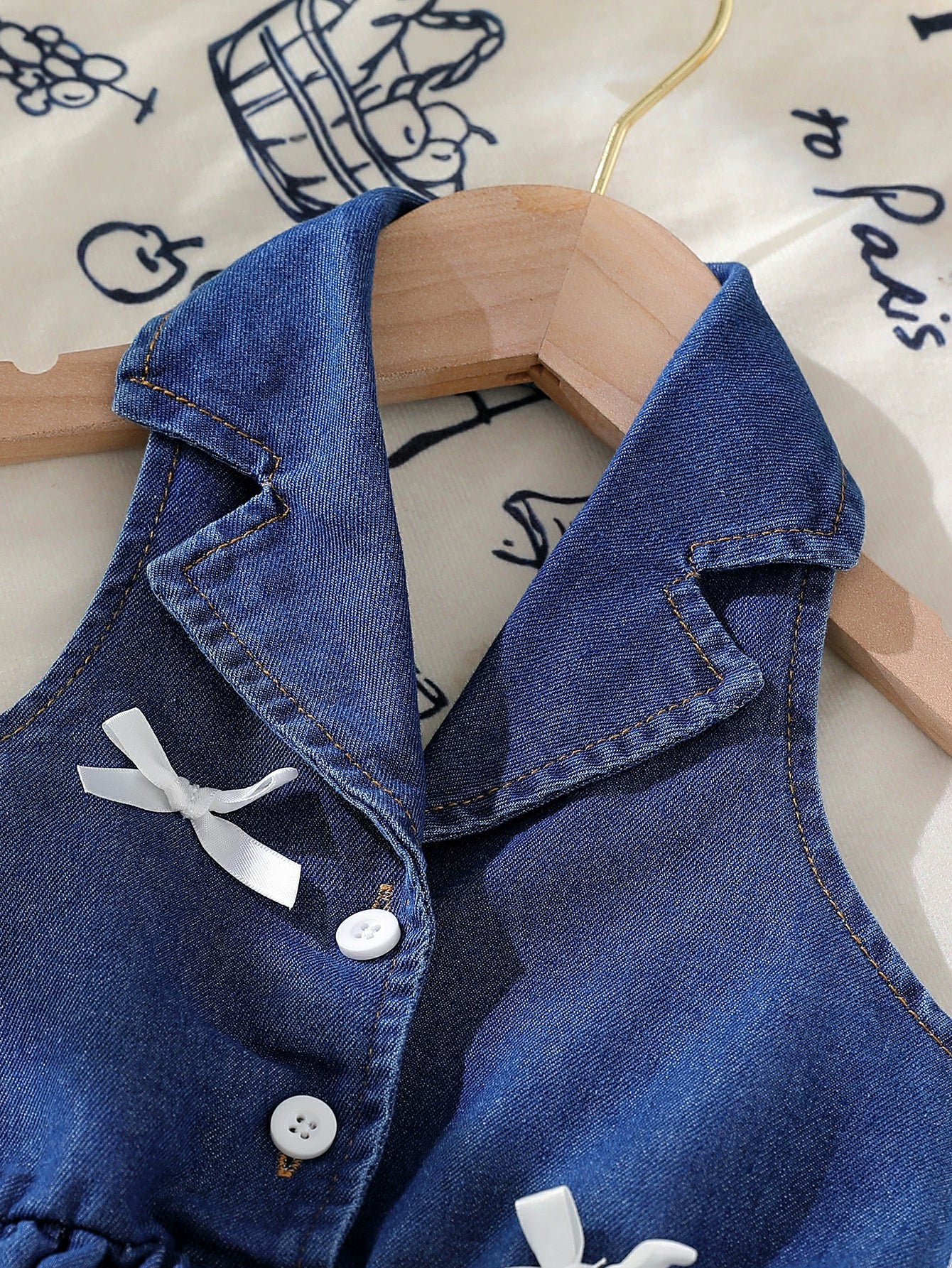 Dark blue denim sleeveless baby dress with white bowknot details and buttons.