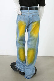 Oversized medium wash denim jeans with bold yellow spray paint effect and raw hems.