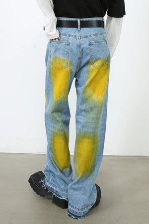 Oversized medium wash denim jeans with bold yellow spray paint effect and raw hems.