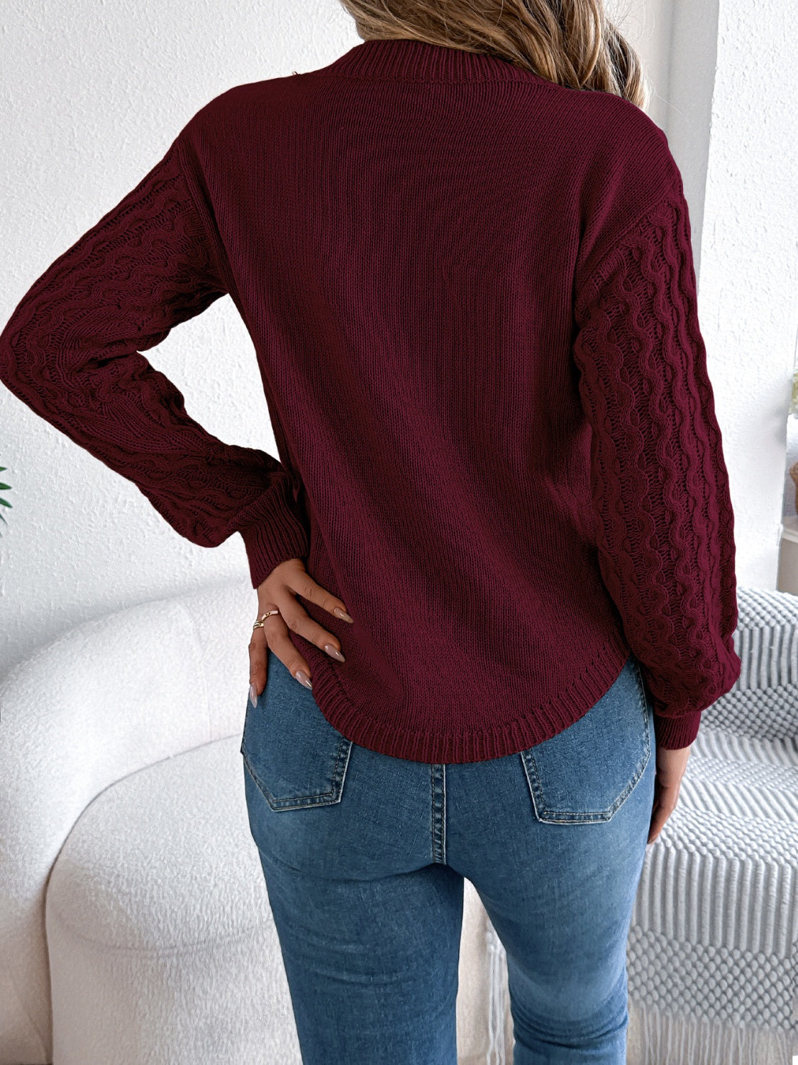 Burgundy acrylic knit sweater with textured cable sleeves and asymmetric hem.