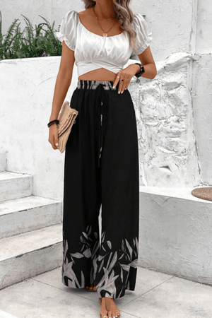 Black wide-leg lounge trousers with botanical print hem and drawstring waist.