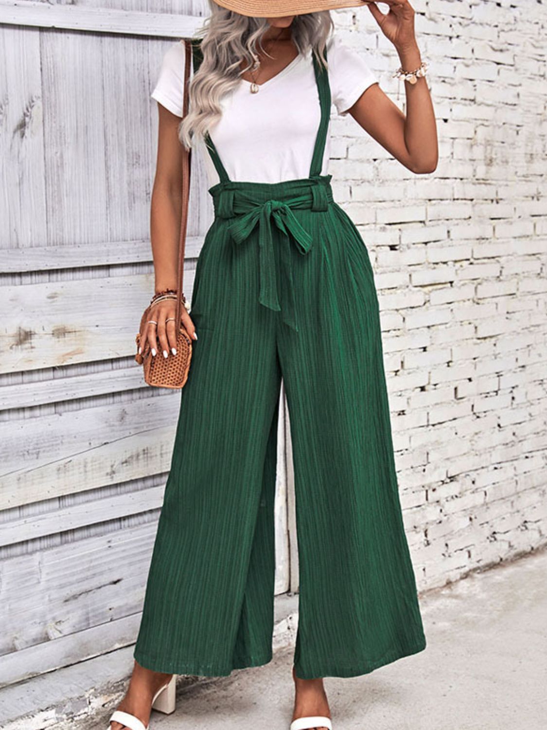 Dark green wide-leg suspender jumpsuit with tie waist and textured fabric.