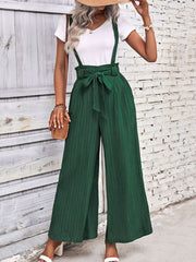 Dark green wide-leg suspender jumpsuit with tie waist and textured fabric.