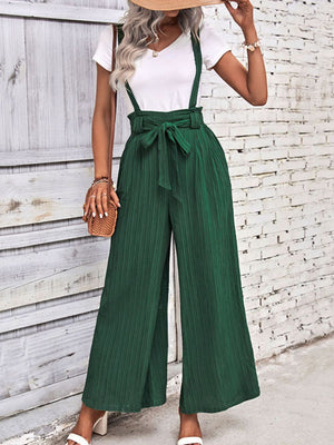 Dark green wide-leg suspender jumpsuit with tie waist and textured fabric.