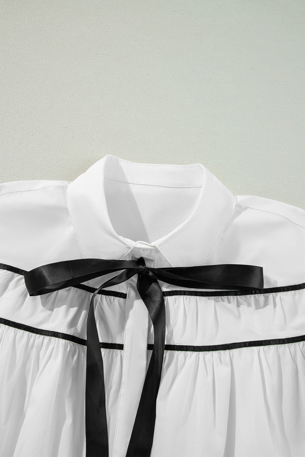 White blouse with black piped trim and a black satin bow detail.