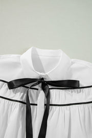 White blouse with black piped trim and a black satin bow detail.