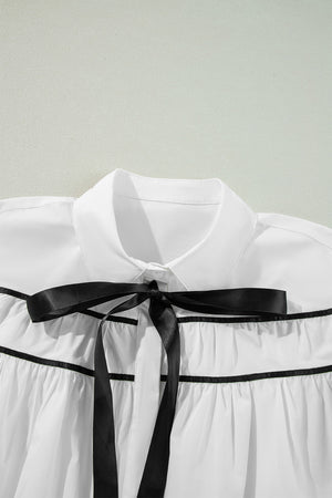 White blouse with black piped trim and a black satin bow detail.
