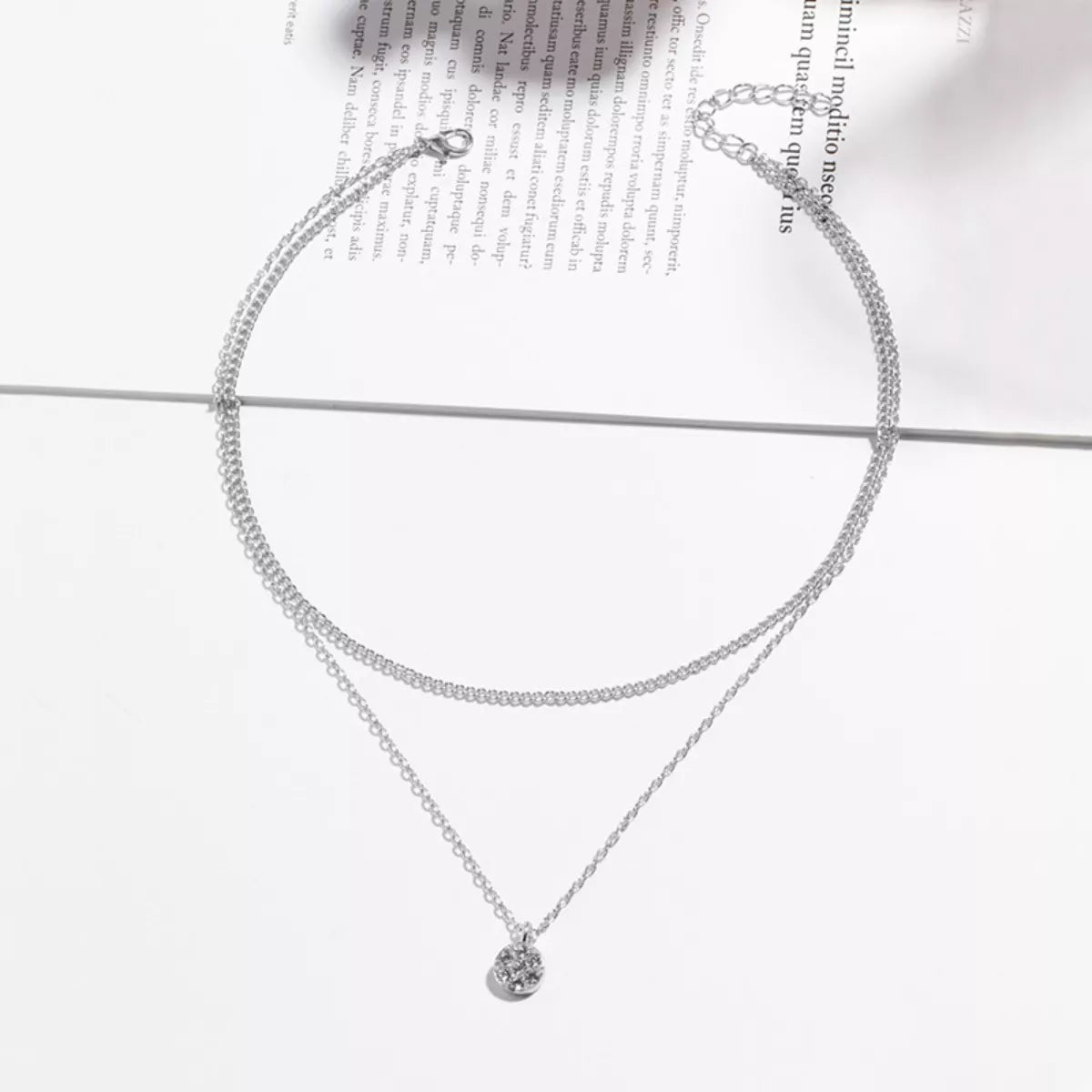 Silver double layered pendant necklace with delicate chains and a small textured pendant.
